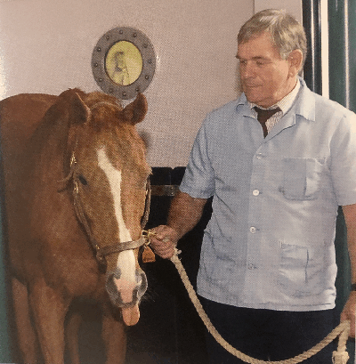 Professor Emeritus Dennis Geiser leads a brown horse that is sticking out their tongue.