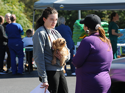 A woman with dog talking to a woman with a bird on her shoulder.