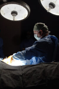Dr. Steve Adair wearing a blue surgery gown operating with bright lights in surgery.