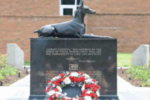 A red, white, and blue floral wreath lays at the foot of the War Dog Memorial located in front of the University of Tennessee College of Veterinary Medicine.