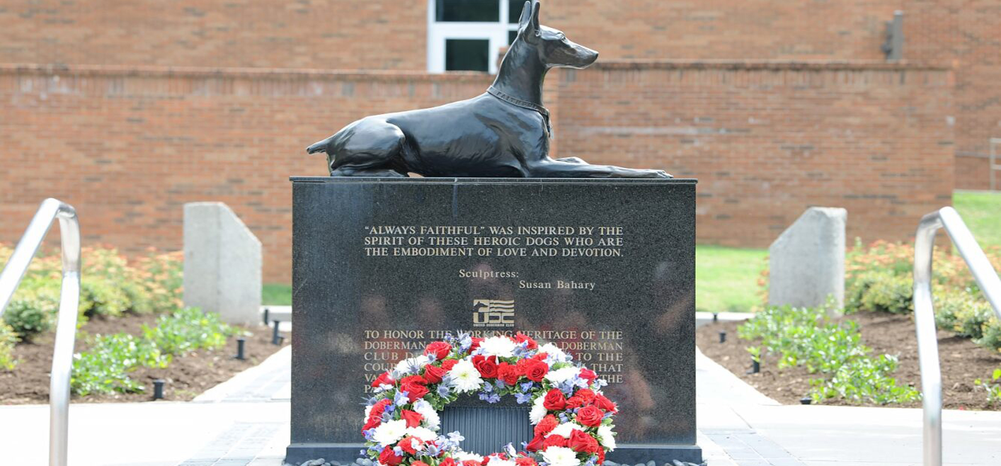 A red, white, and blue floral wreath lays at the foot of the War Dog Memorial located in front of the University of Tennessee College of Veterinary Medicine.